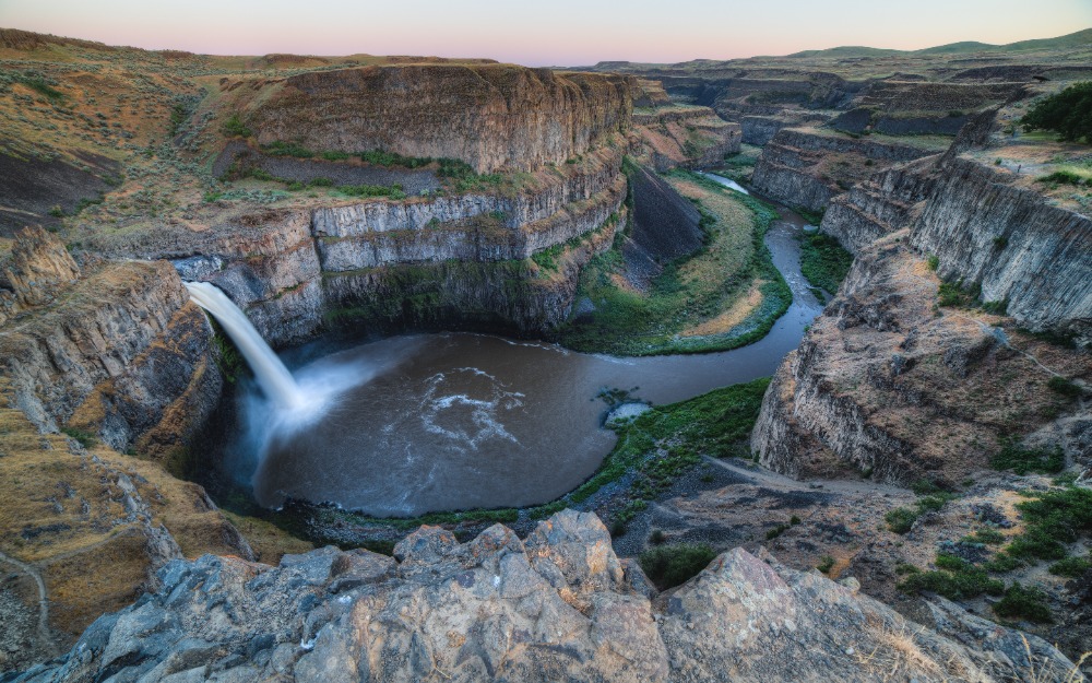 tall waterfall flowing into large river mouth in canyon