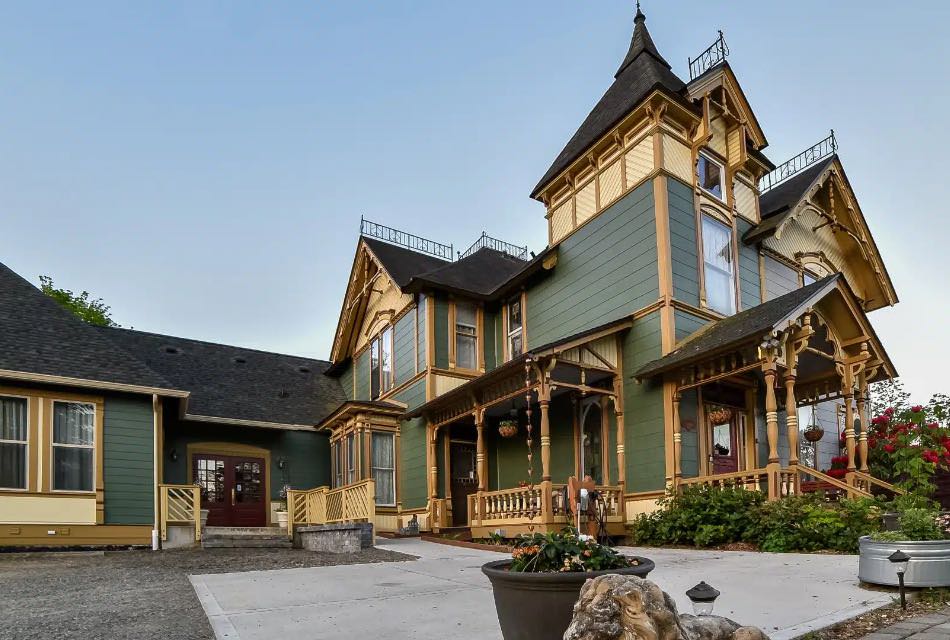 Exterior view of property painted dark green with dark mustard trim, covered front entry, concrete driveway, and multiple flower gardens