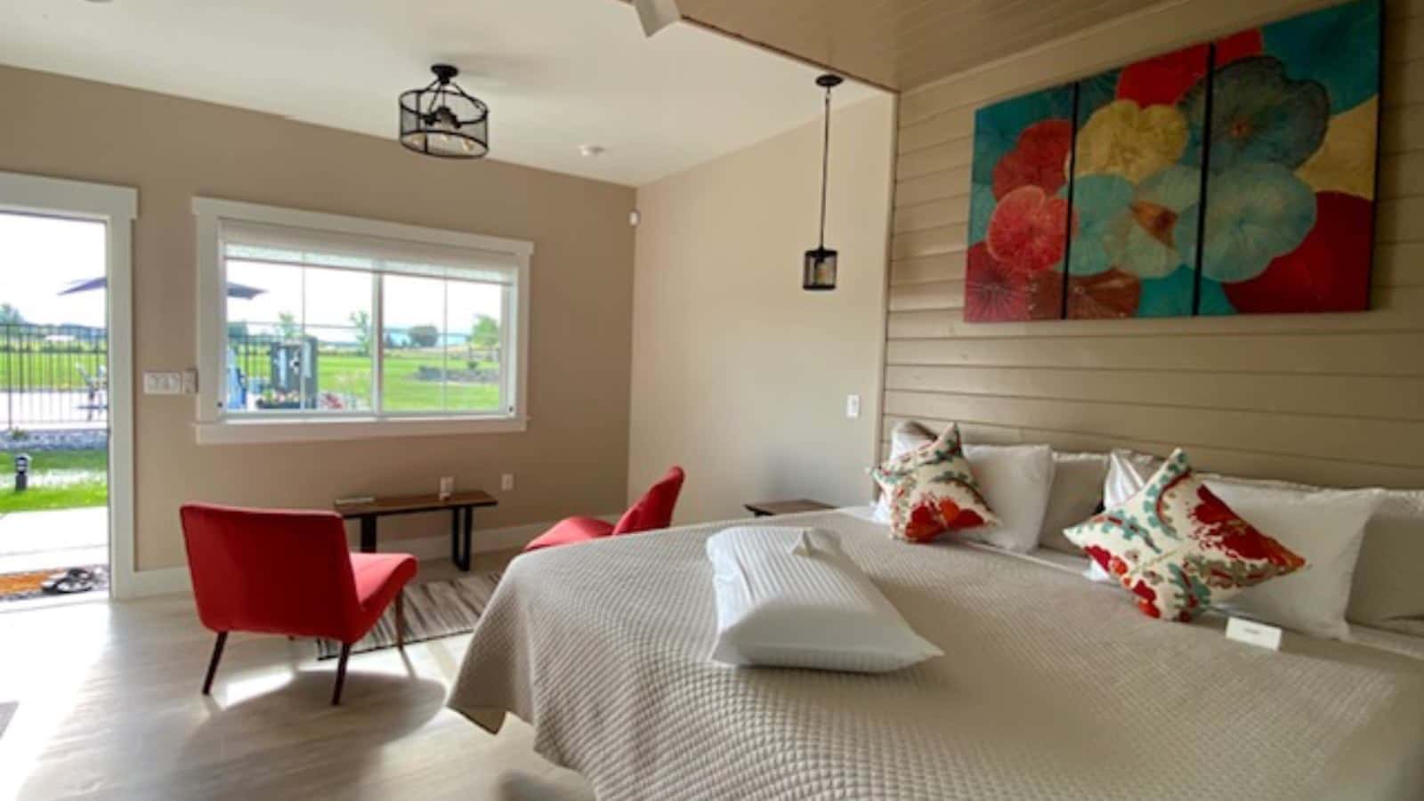 Bedroom with cream walls, white trim, hardwood flooring, cream bedding, sitting area, and view of the pool area