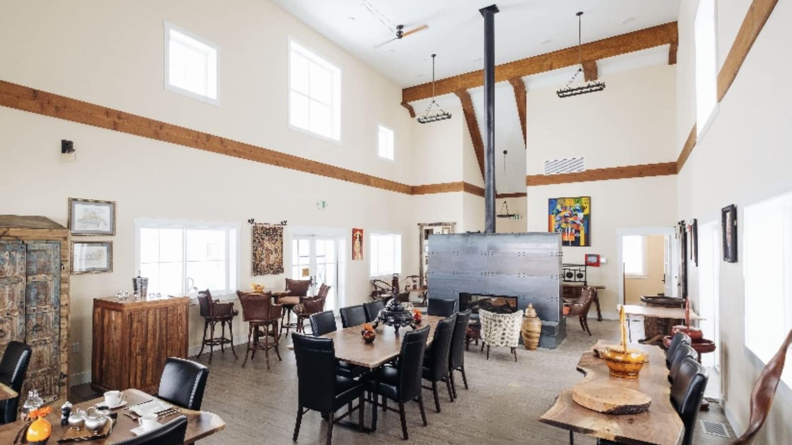 Great room with white walls, white trim, hardwood flooring, vaulted ceilings, wooden dining tables with chairs, and metal fireplace