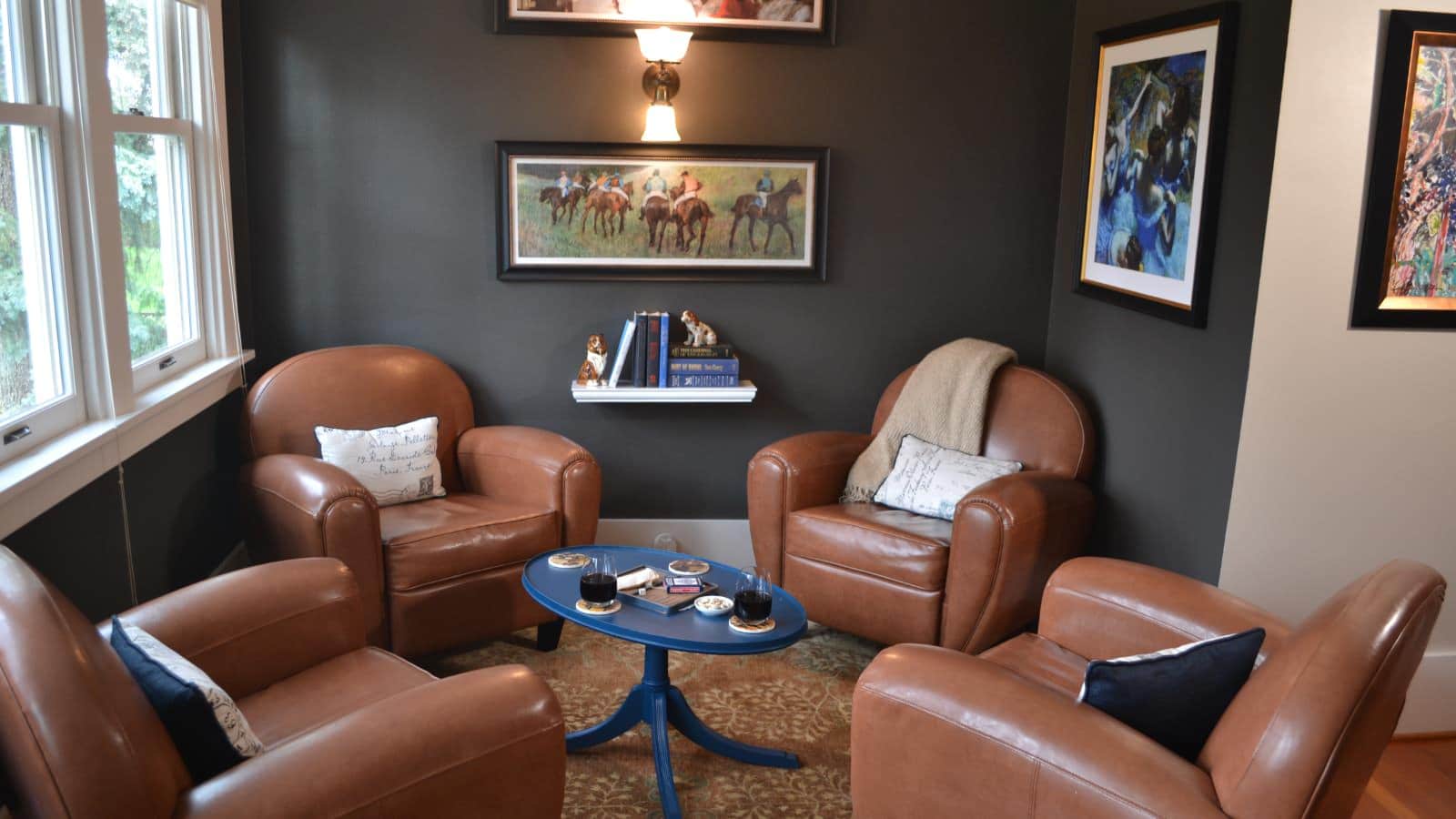 Living room with dark gray walls, white trim, hardwood flooring, light brown leather armchairs, and small blue table