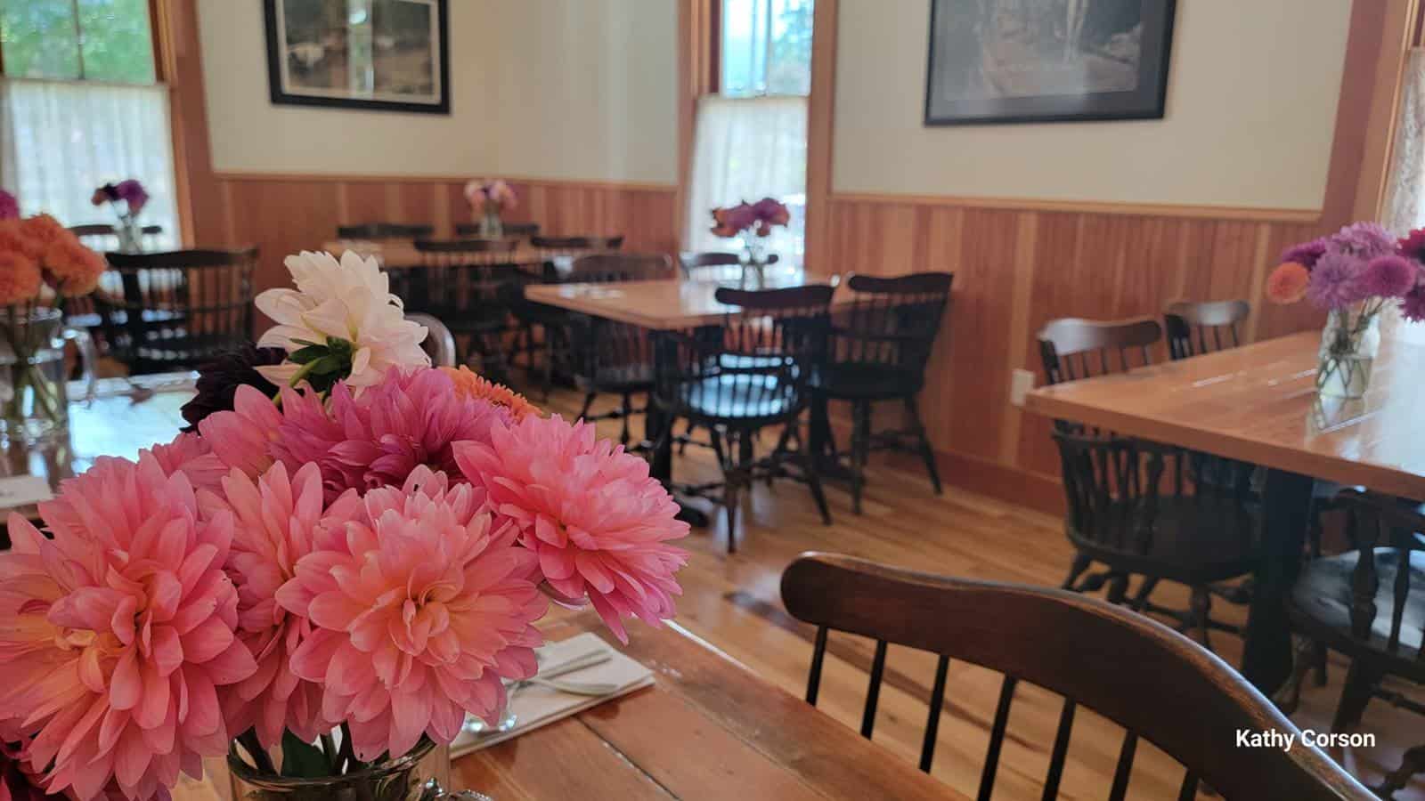 Close up view of pink flowers in a vase on a wooden table in a dining room with white walls and natural wooden wainscotting