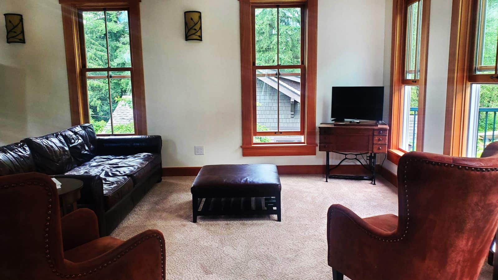 Living room with white walls, wooden trim, light tan carpeting, black leather couch, leather coffee table, and dark red velvet upholstered antique armchairs