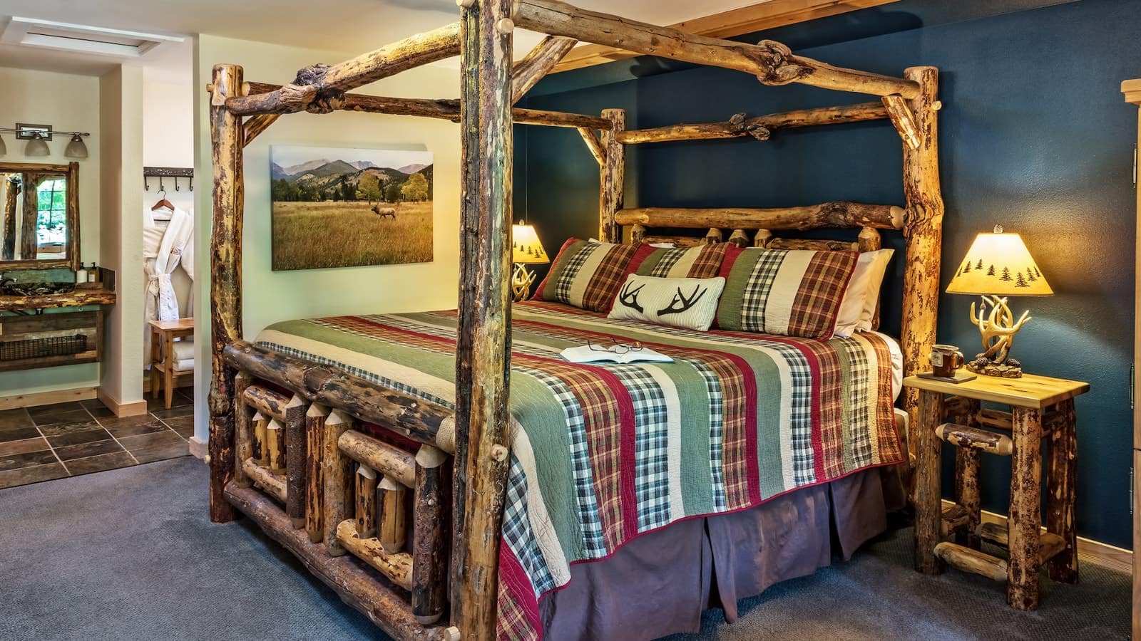 Bedroom with navy blue accent wall, carpeting, log canopy bed, multicolored bedding, and log nightstands with antler lamps