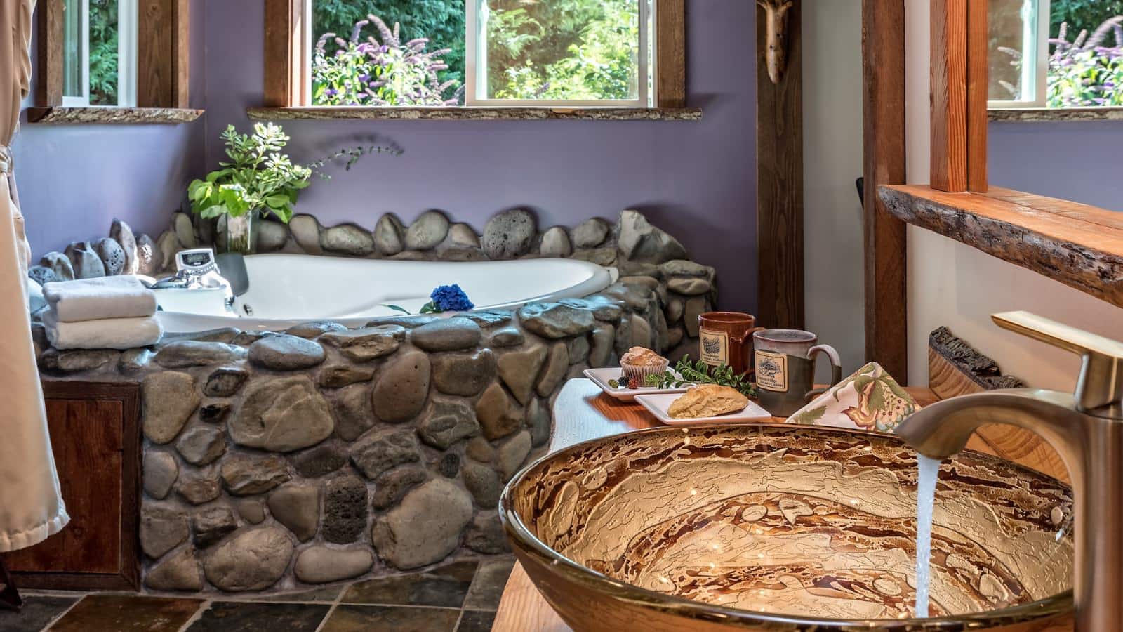 Close up of large custom bowl used as sink basin with large stone covered soaking tub in the background