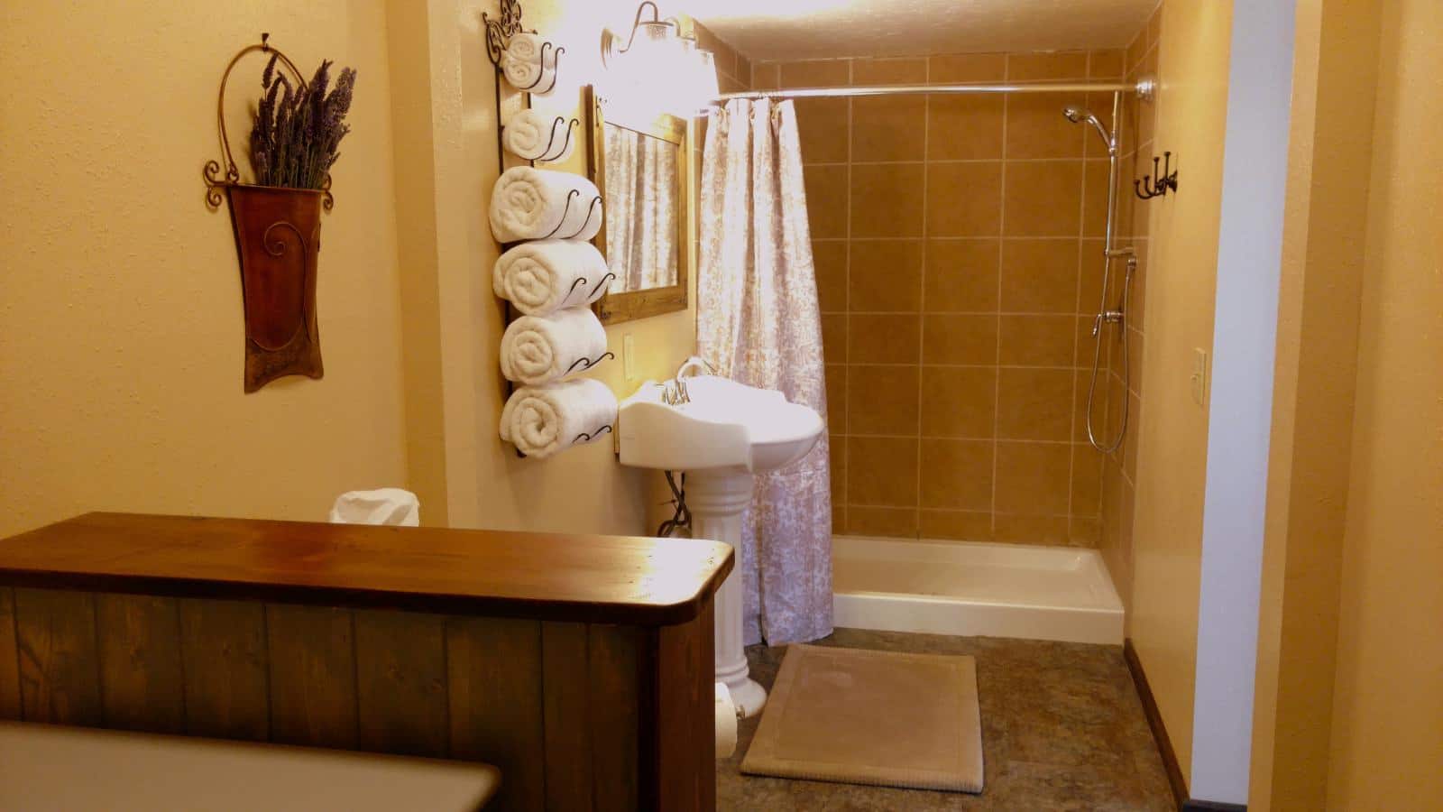 Bathroom with cream walls, laminate flooring, tiled walk-in shower with curtain, and white pedestal sink