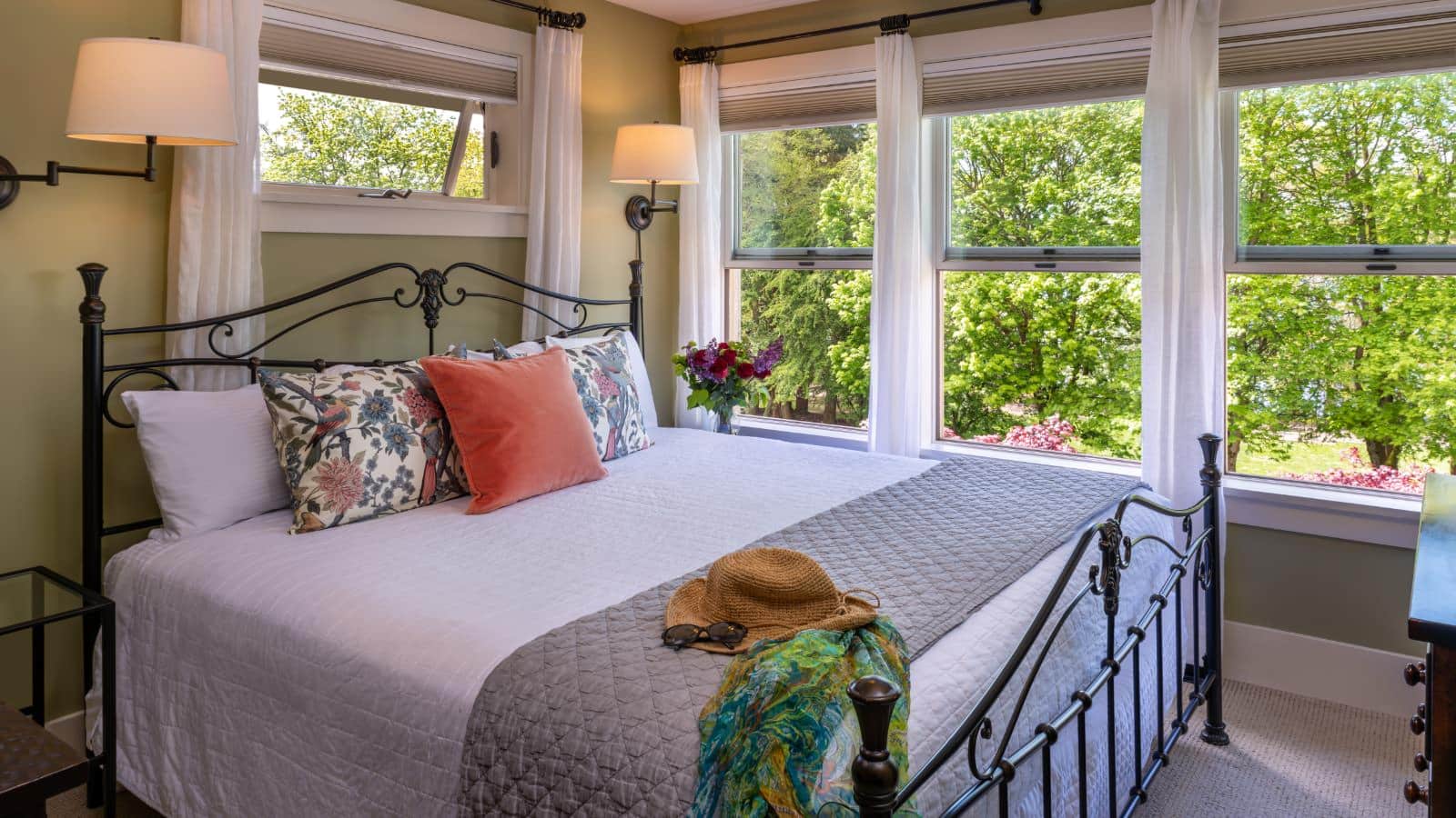 Bedroom with light green walls, carpeting, wrought iron bed, white bedding, and large windows with views to the outside