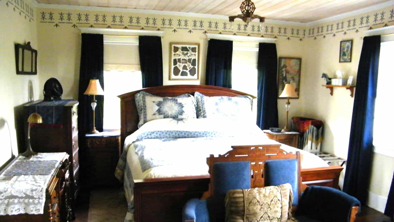 Bedroom with cream walls, hardwood flooring, wooden bed, multicolored bedding, wooden dressers, and dark blue floor length curtains