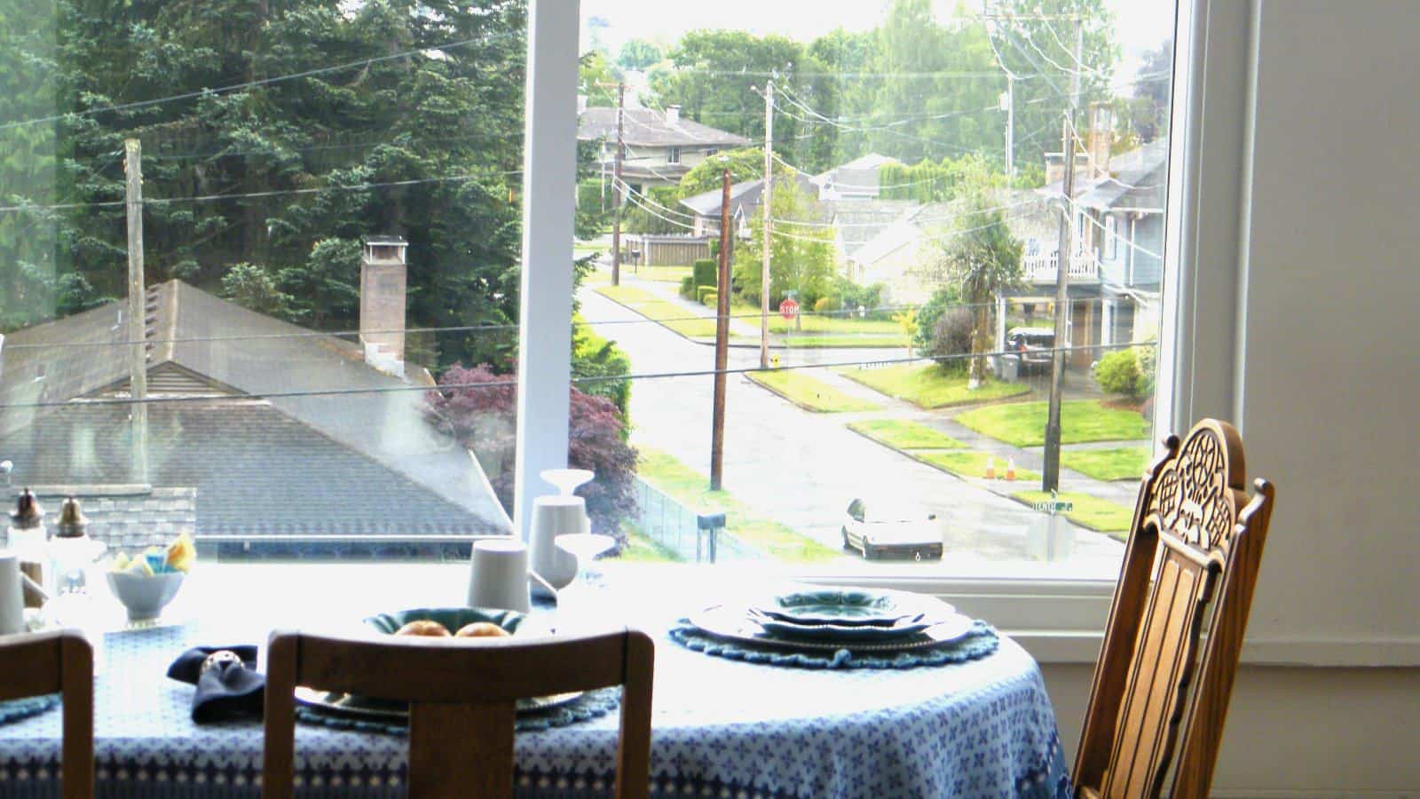 View of dining table with wooden chairs next to large window with view of the neighborhood