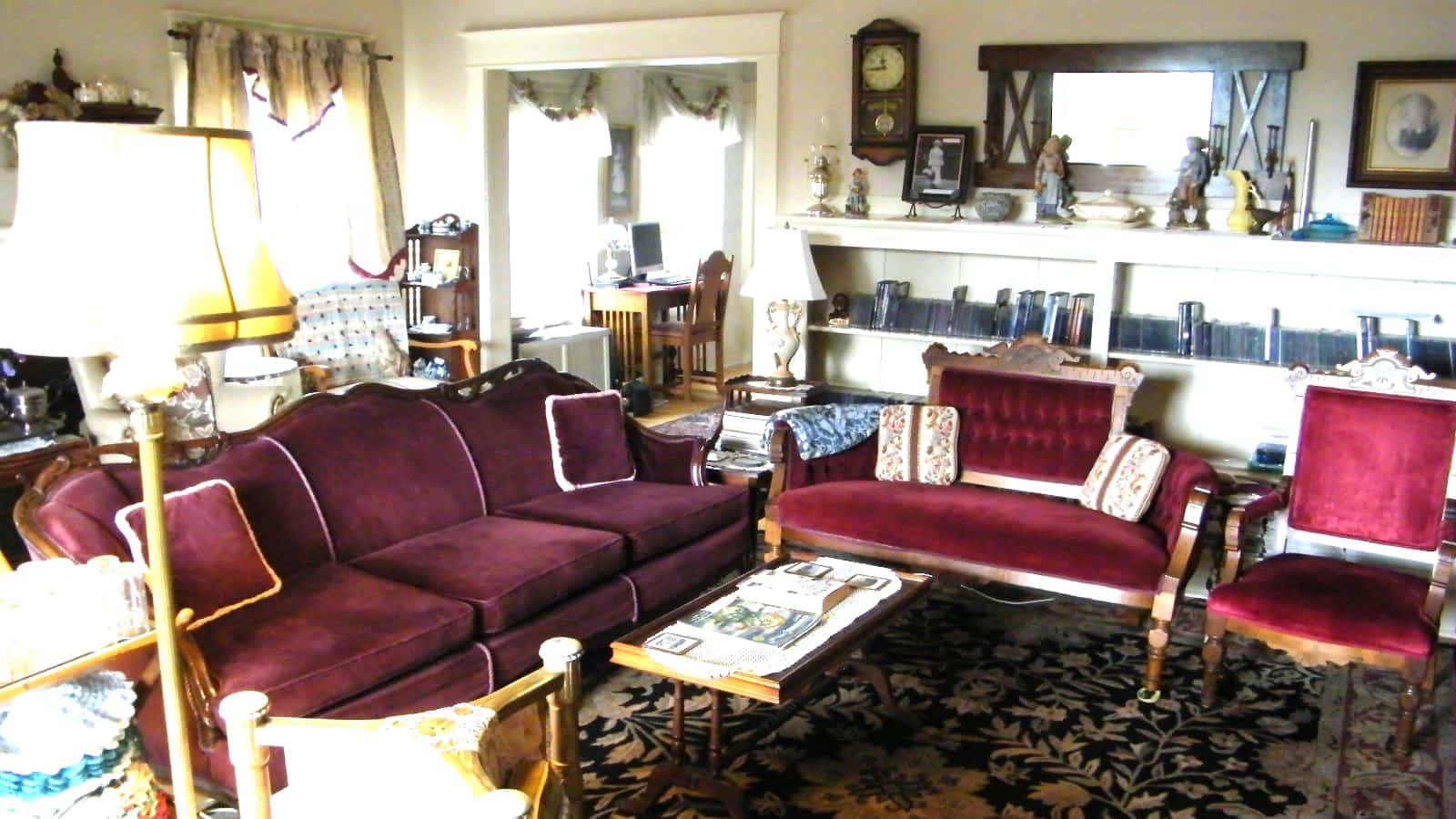 Living room with white walls, hardwood flooring, and red velvet upholstered antique sofa, love seat, and chairs