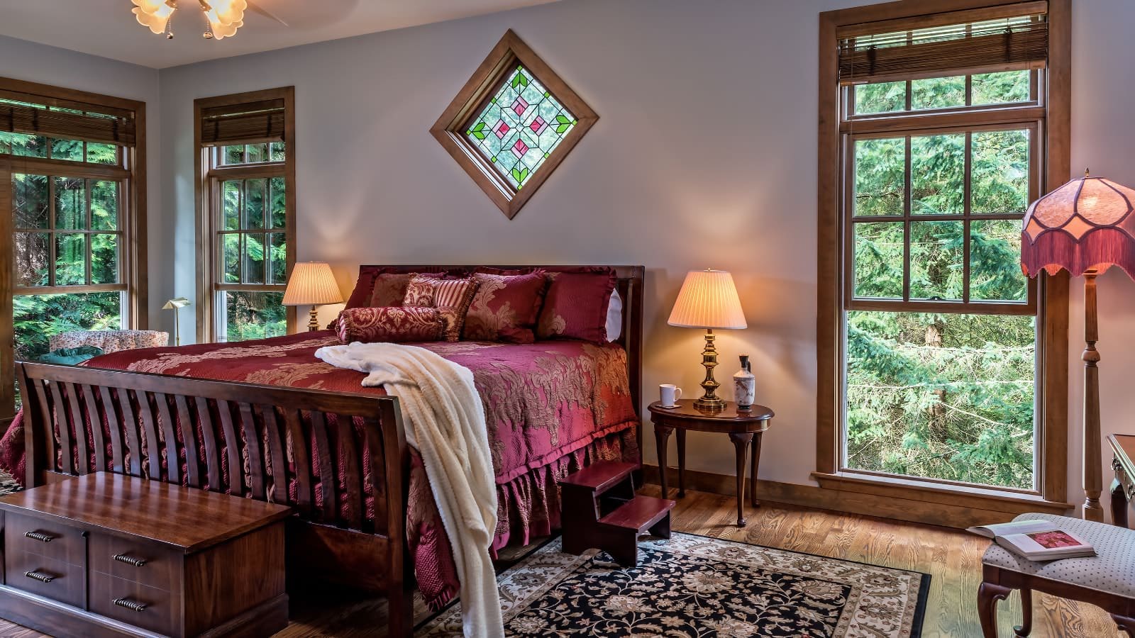 Bedroom with light lavender walls, hardwood flooring, dark wooden sleigh bed, burgundy bedding, and large windows with views of the outside