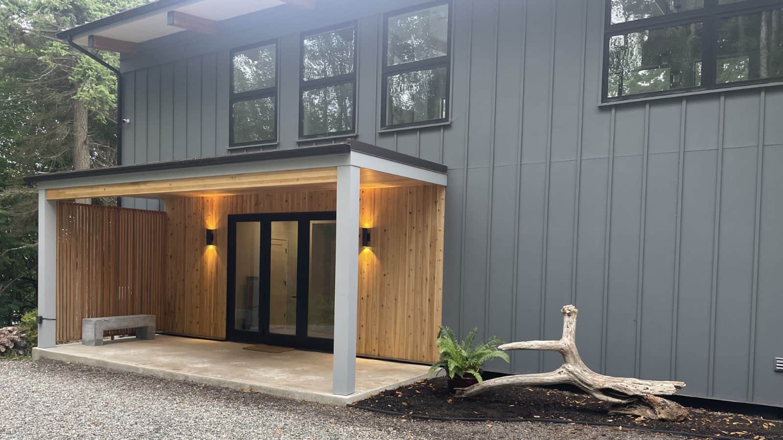 Exterior view of property painted dark gray with covered front entry of natural wood surrounding glass doors with black trim