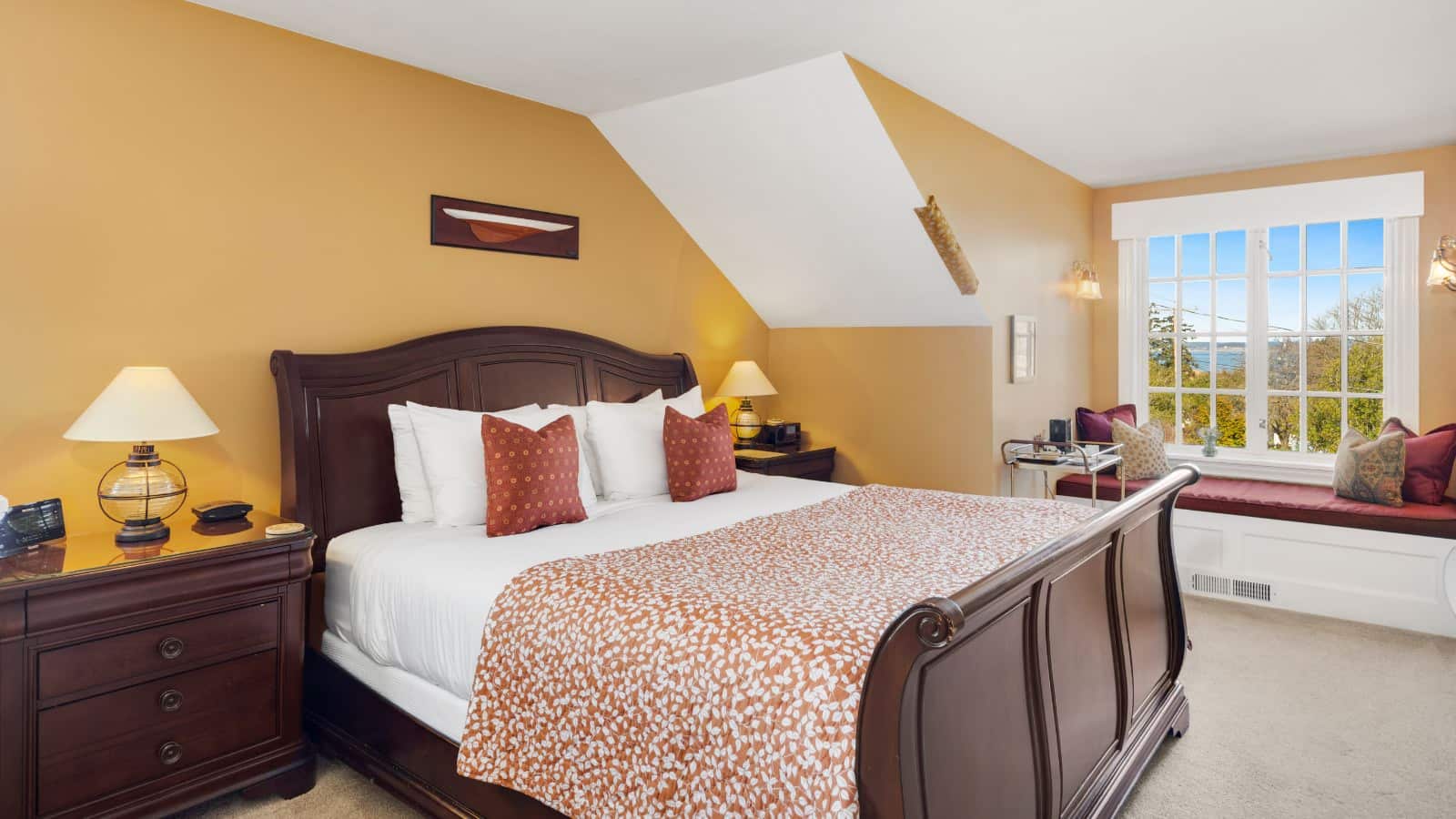 Bedroom with light orange walls, light tan carpeting, wooden sleigh bed, white bedding, dark wooden dresser, and large window