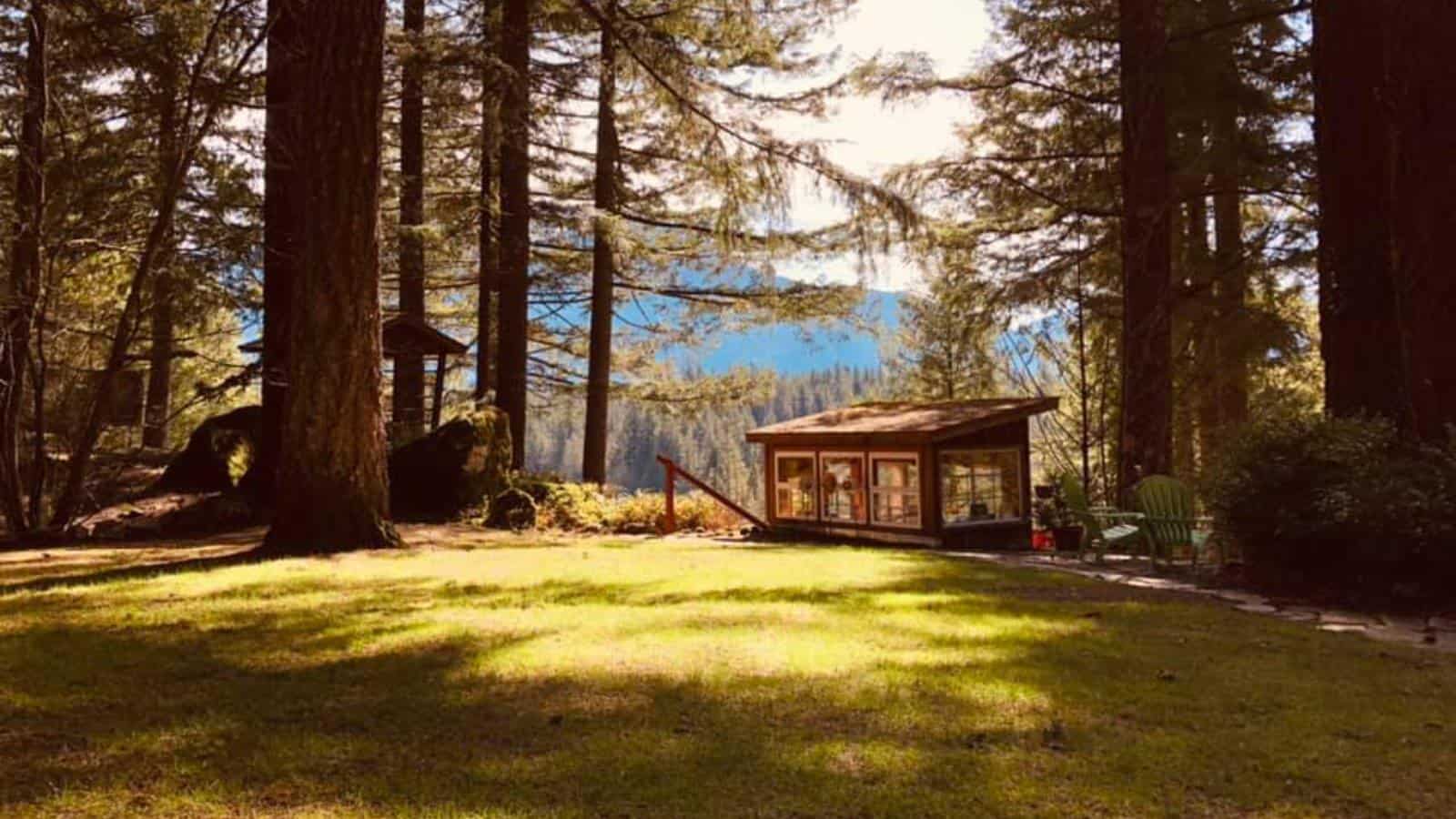 Exterior view of property buildings painted brown surrounded by green grass, large trees, and mountains in the background