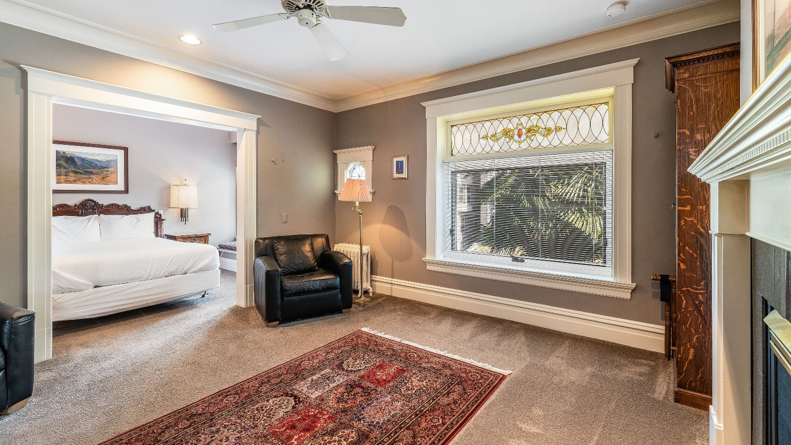 Bedroom suite with gray walls, white trim, light tan carpeting, black leather armchairs, fireplace, wooden bed, and white bedding