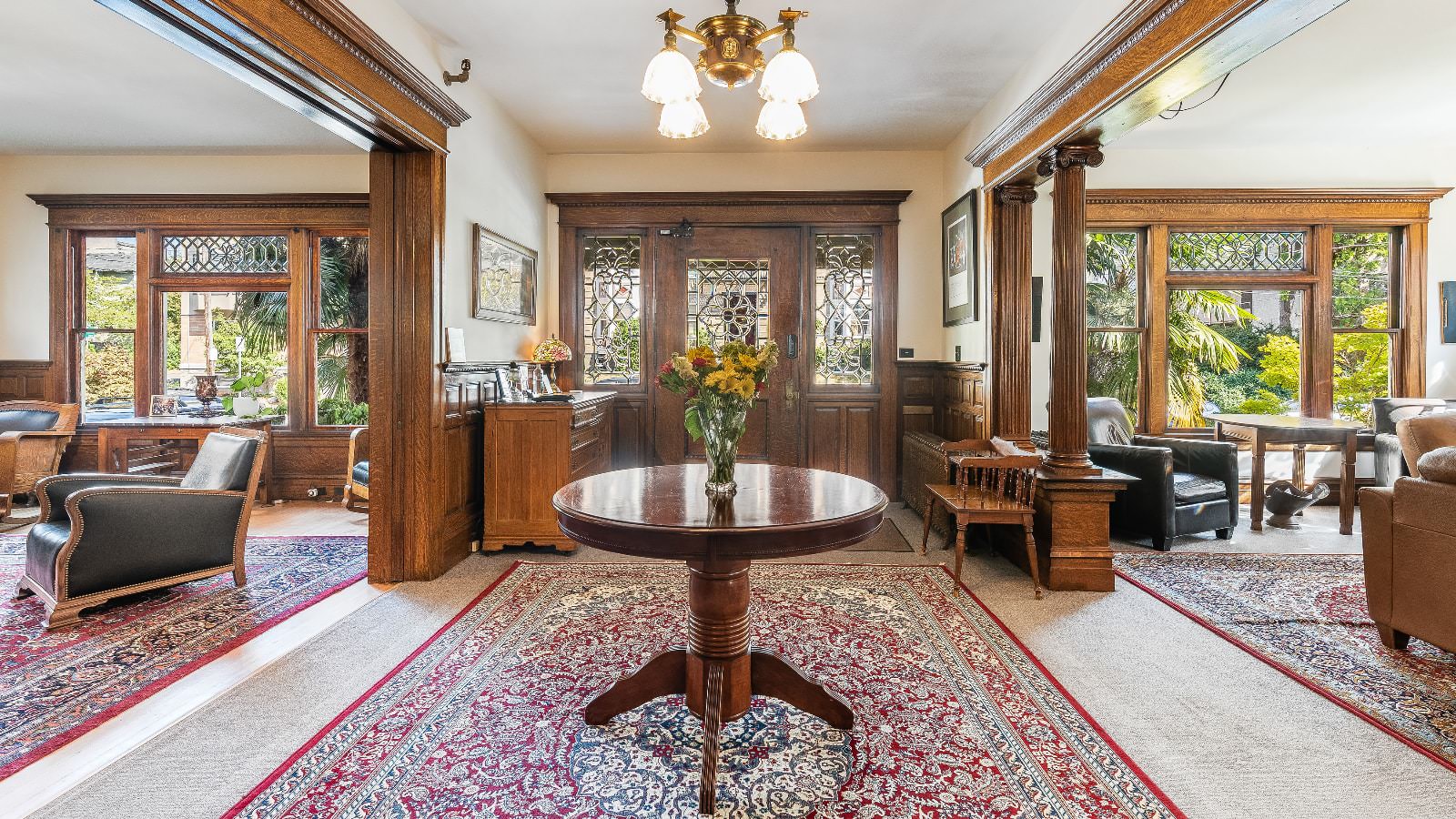 Front entry with rooms on both sides all with white walls, light carpeting, wooden trim, wooden doors, large windows, and wooden furniture