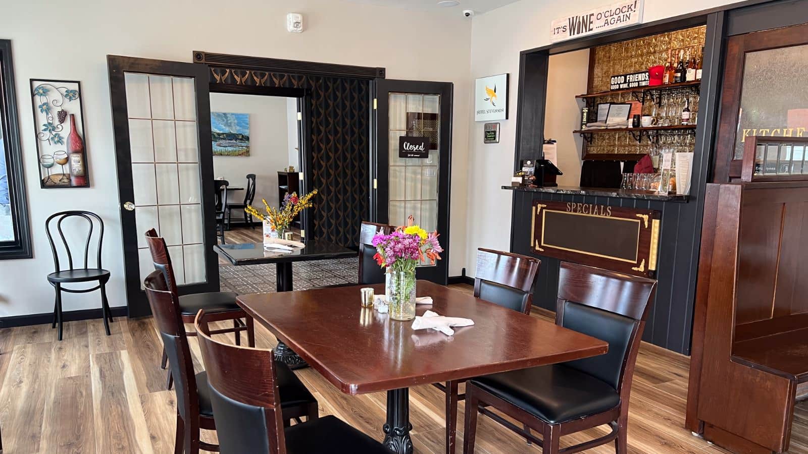 Dining area with white walls, black trim, hardwood flooring, wooden tables and chairs, and small bar area