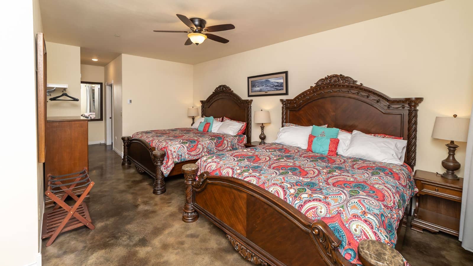 Bedroom with cream walls, two dark wooden beds, multicolored paisley bedding, and dark wooden nightstands with lamps