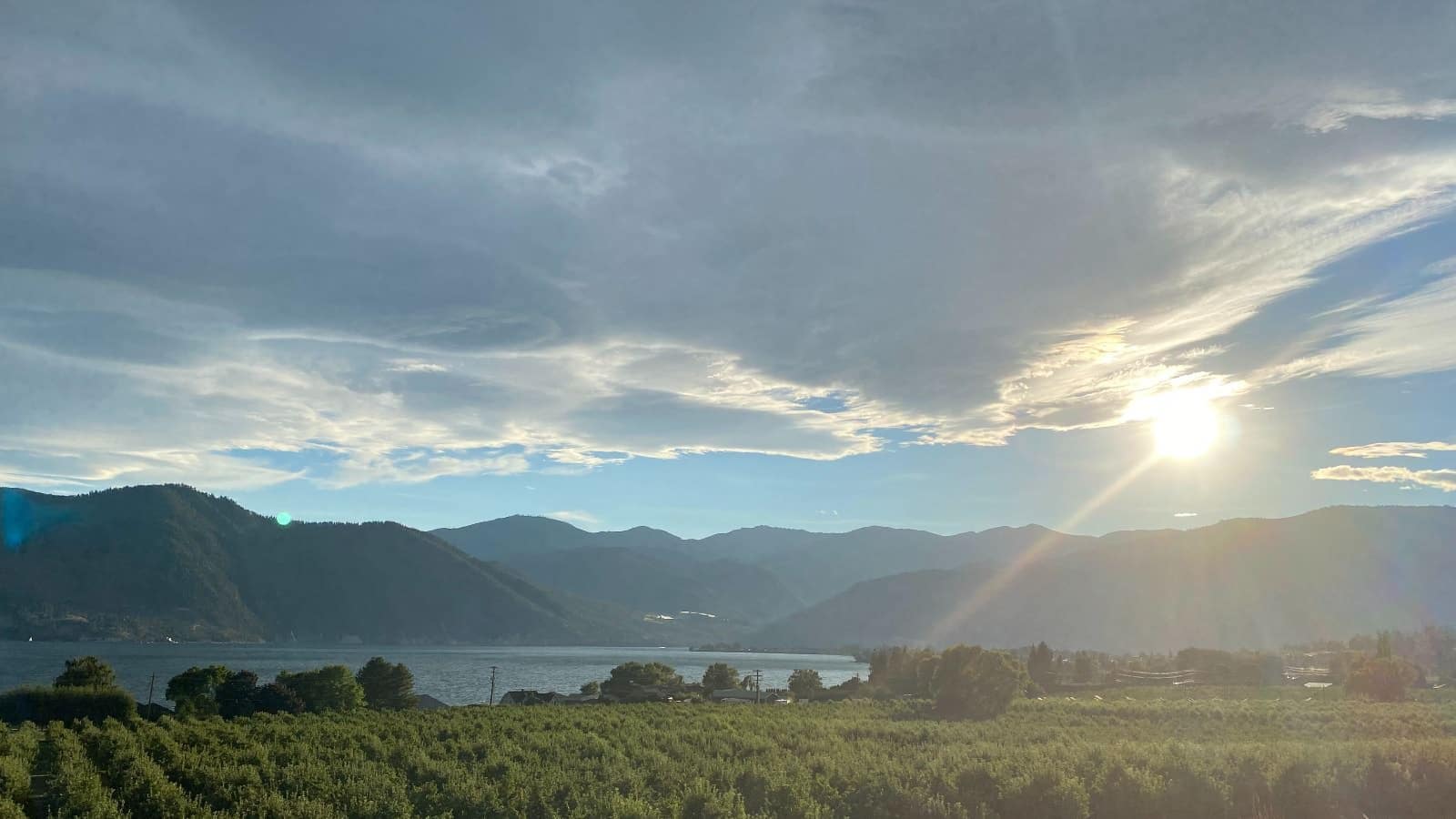 Large field with a body of water and mountains in the background and setting sun