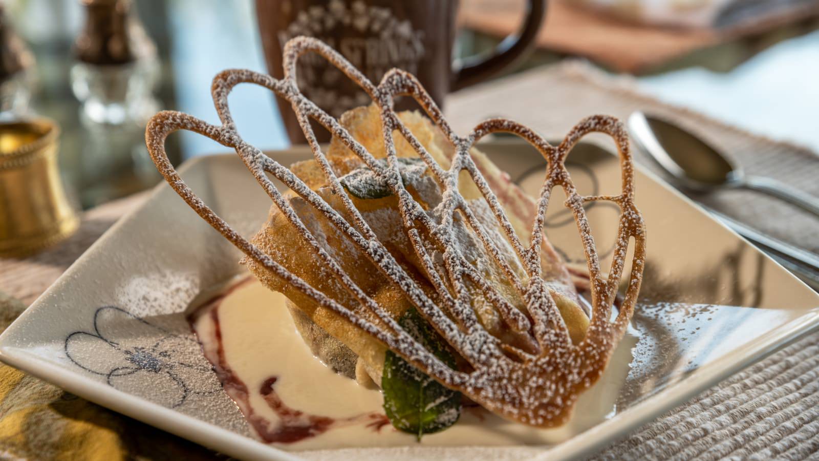 Close up view of a fancy dessert dusted with powdered sugar on white pentagon shaped plate