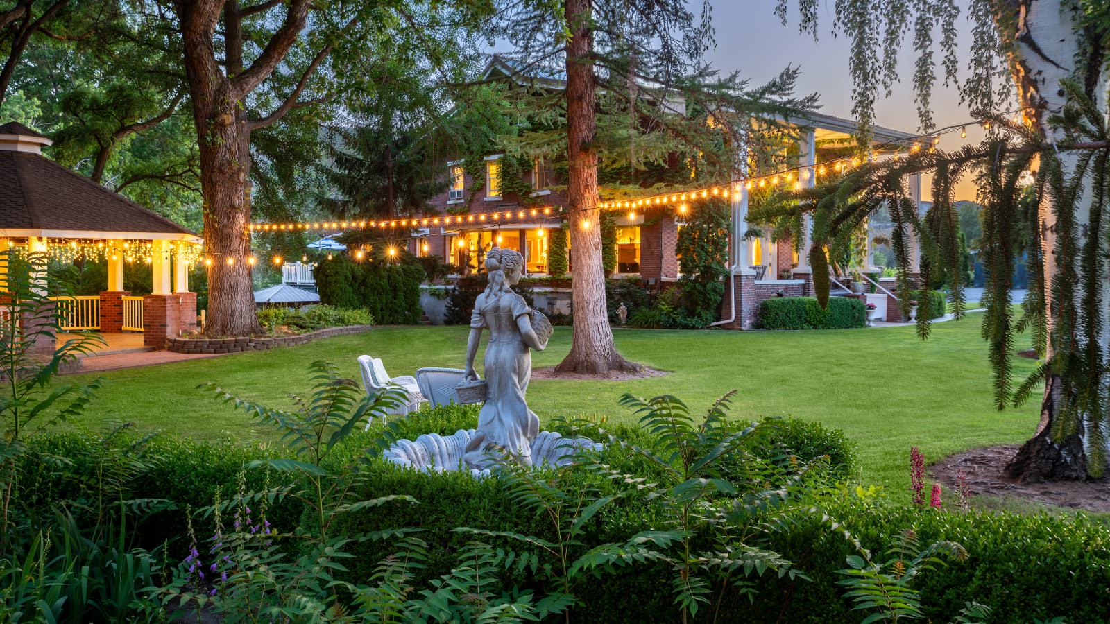 Large backyard of property with green grass, flower beds, gazebo, statue, and string lights