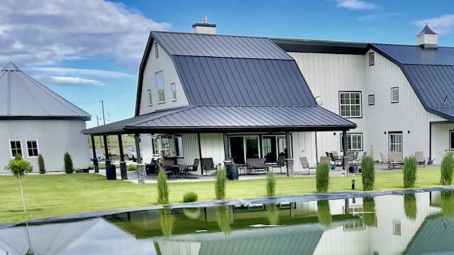 Exterior view of the property painted white with black trim, black roof, large covered porch, and large green lawn