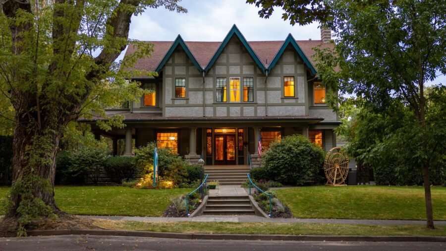 Exterior view of property painted light gray with taupe trim surrounded by green grass, shrubs, and trees