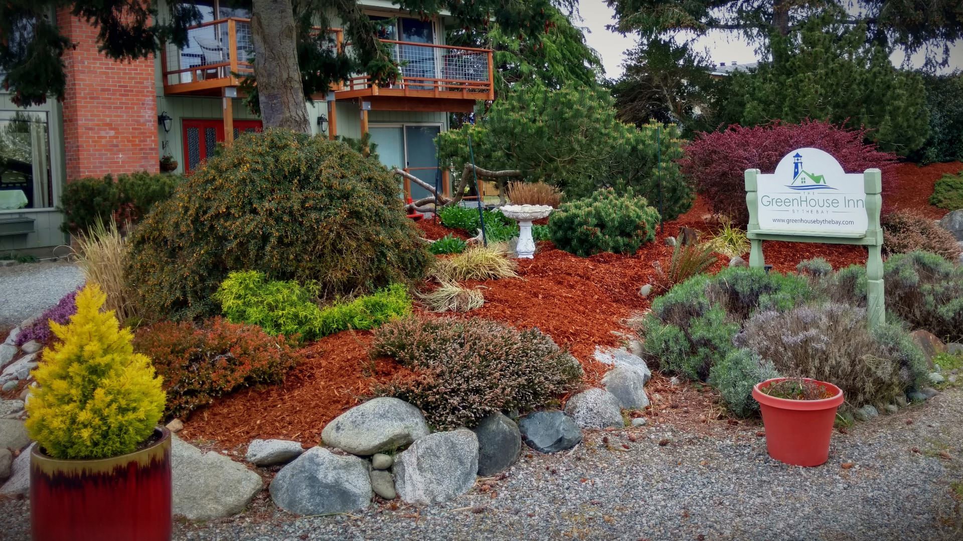 Exterior view of the property painted light green surrounded by light gray pea gravel, multicolored bushes, and green trees