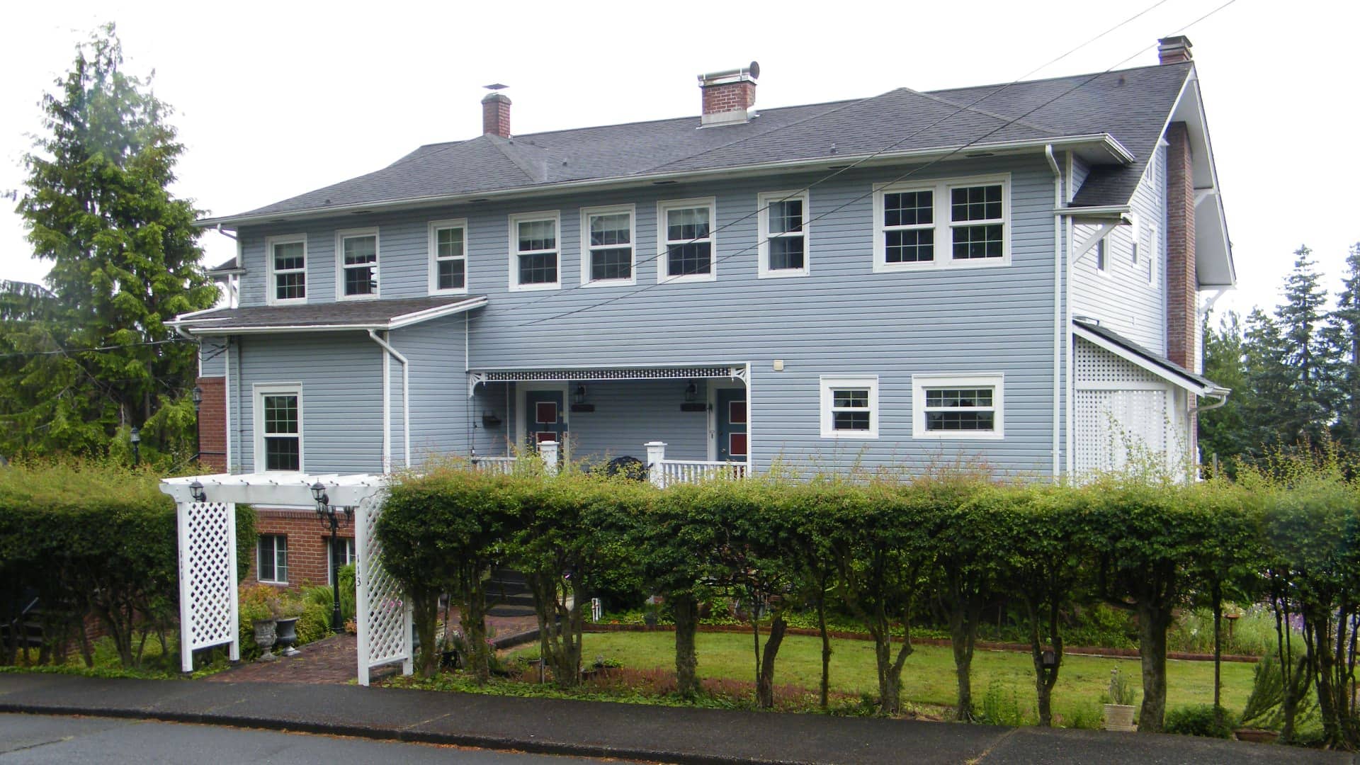 Exterior view of property painted light blue with white trim surrounded by green grass, shrubs, and trees