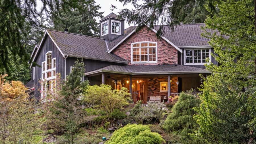 Exterior view of property with red and black brick, gray siding, white trim, and surrounded by green shrubs and trees