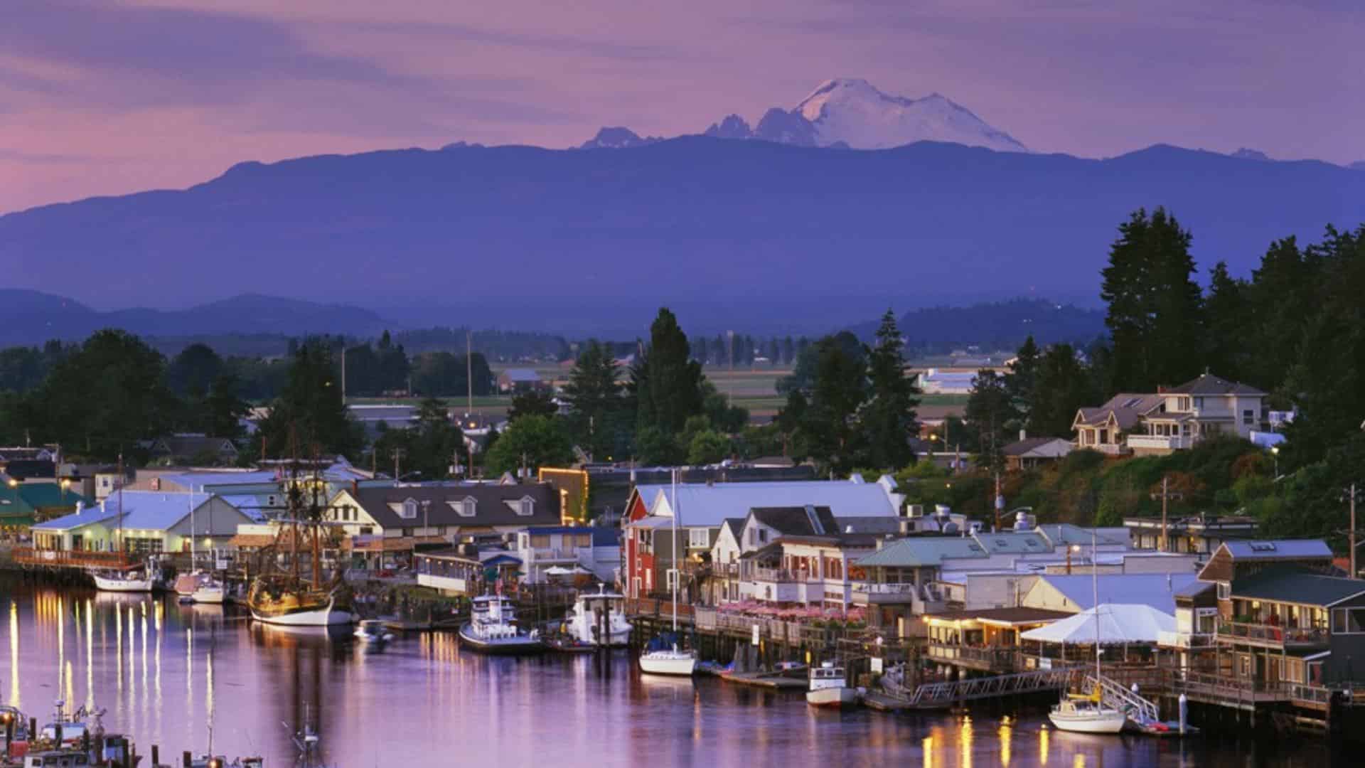 Small town with multiple boats docked on calm water with a large mountain in the background