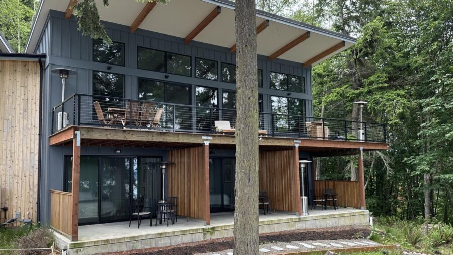 Exterior view of property painted dark gray with natural wood decking elements separating each rooms patio surrounded by large green trees