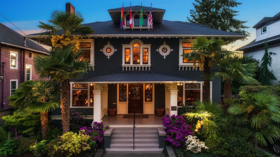 Exterior view of property painted dark green, white trim, covered front entrance, and surrounded by purple and white flowering bushes, green shrubs, and trees