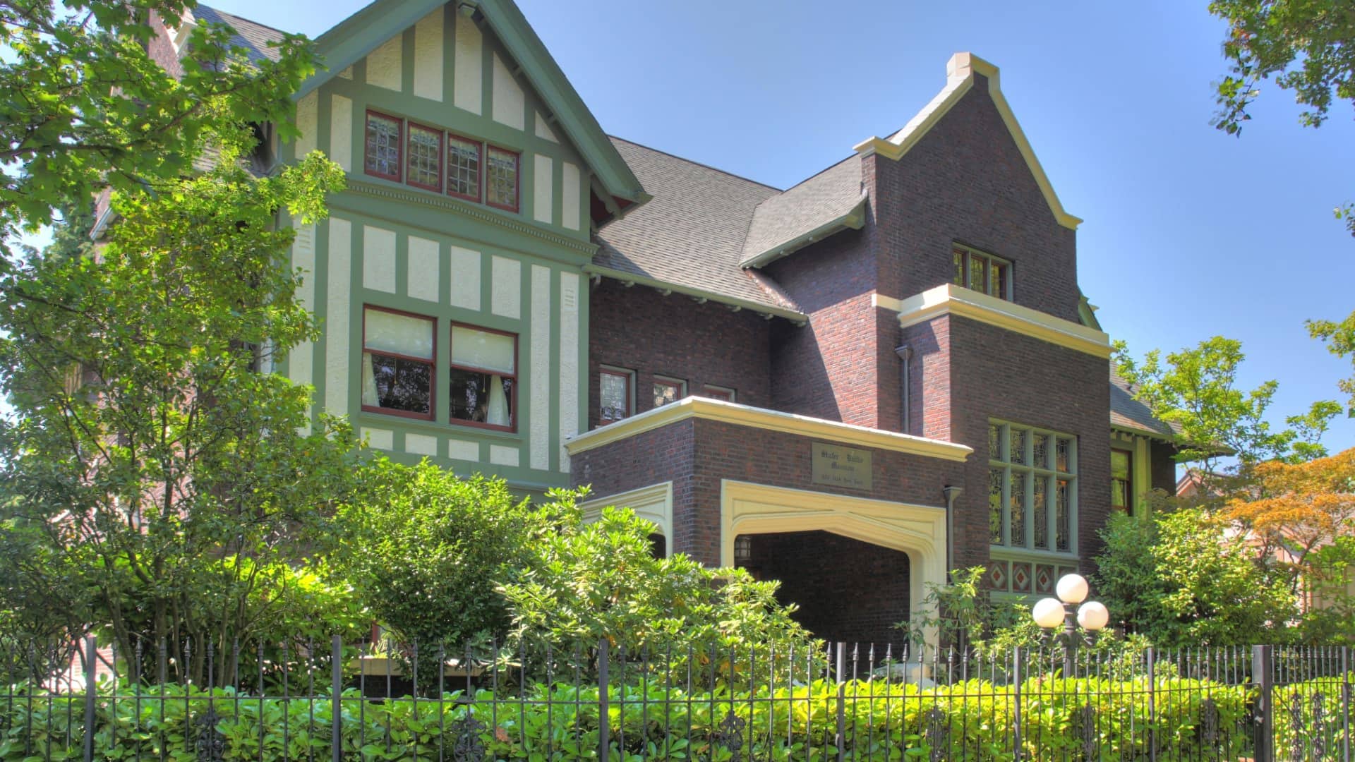 Exterior view of property with red and brown brick and pops of almond and sage green trim surrounded by green shrubs and trees