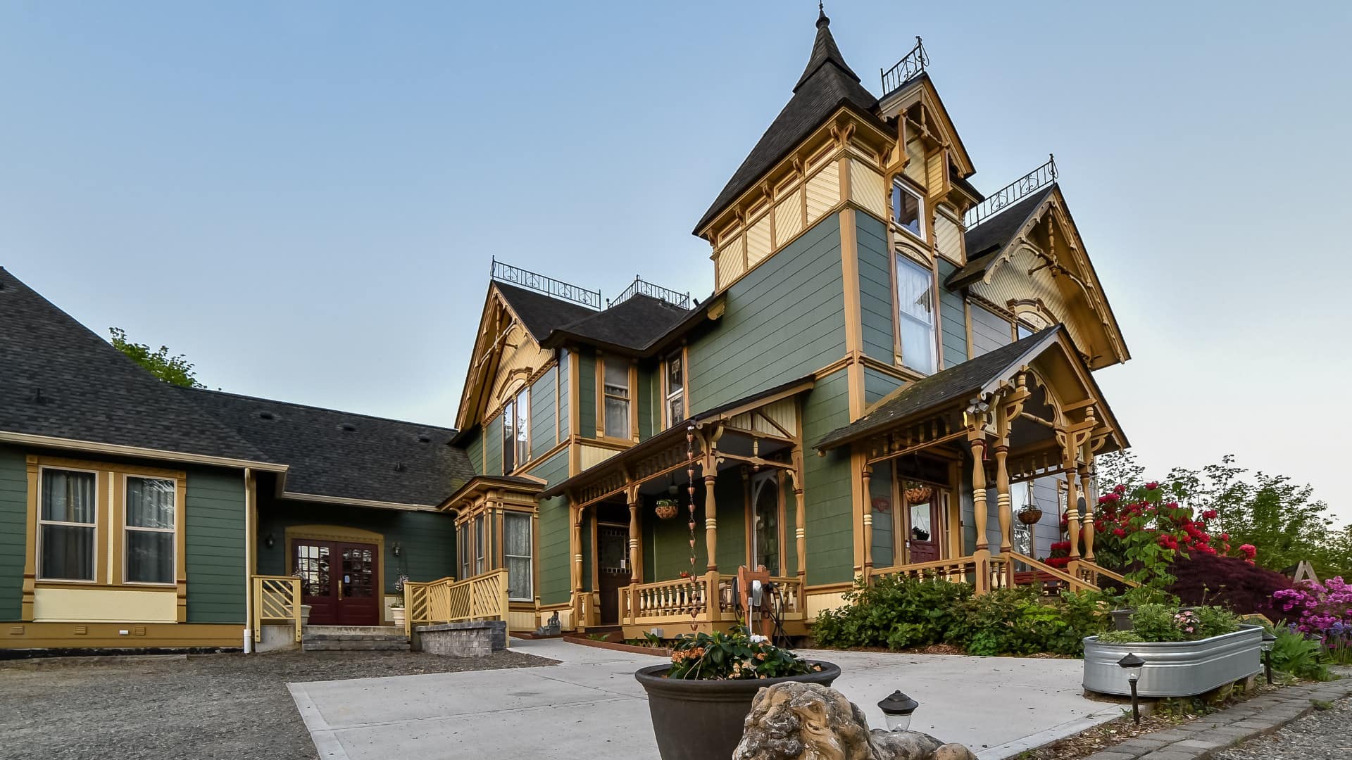 Exterior view of property painted dark green with dark mustard trim, covered front entry, concrete driveway, and multiple flower gardens