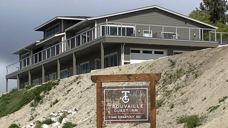 Exterior view of property painted dark gray with white trim with second level wrap-around deck all sitting on top of a rocky hill