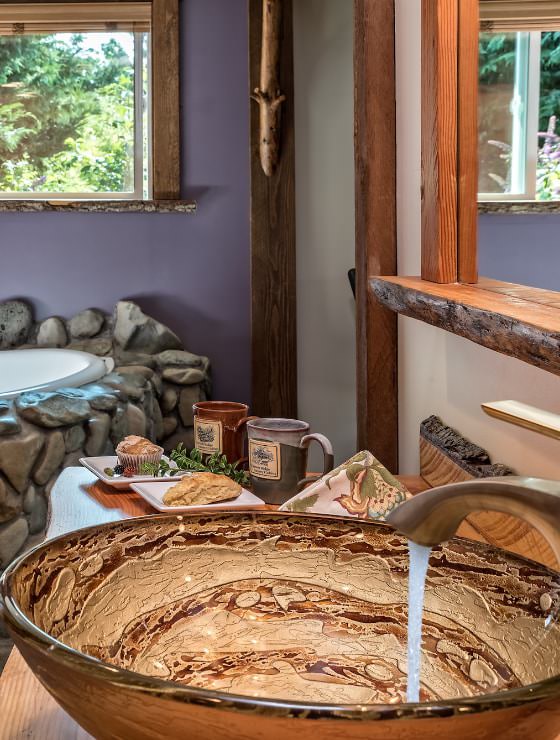 Close up of large custom bowl used as sink basin with large stone covered soaking tub in the background