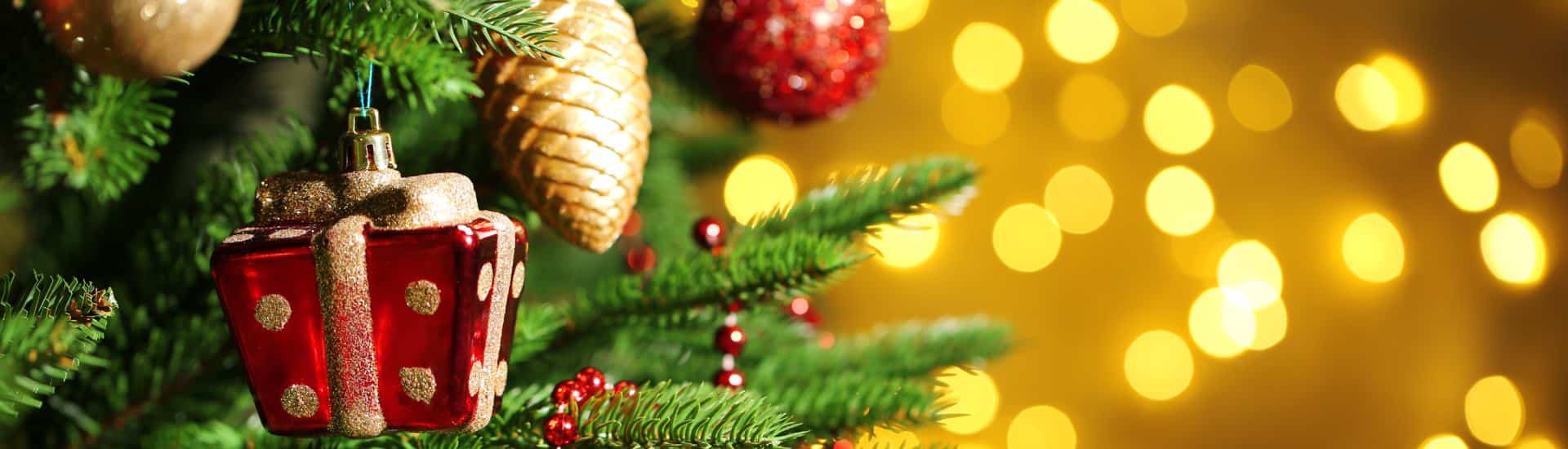 Close up of Christmas tree branches with large glass ornaments of pine cones, balls, and presents