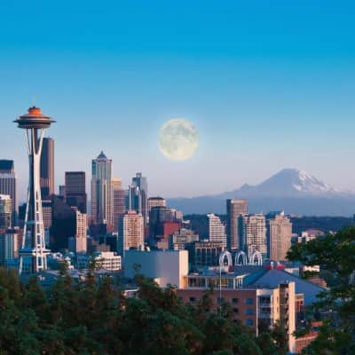 Downtown city view of Seattle with multiple buildings including the Space Needle with a mountain and the moon in the background